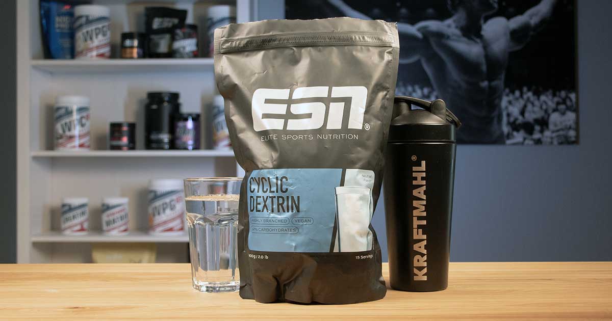 Beutel ESN Cyclic Dextrin neben Kraftmahl Shaker und Glas Wasser auf Holztisch