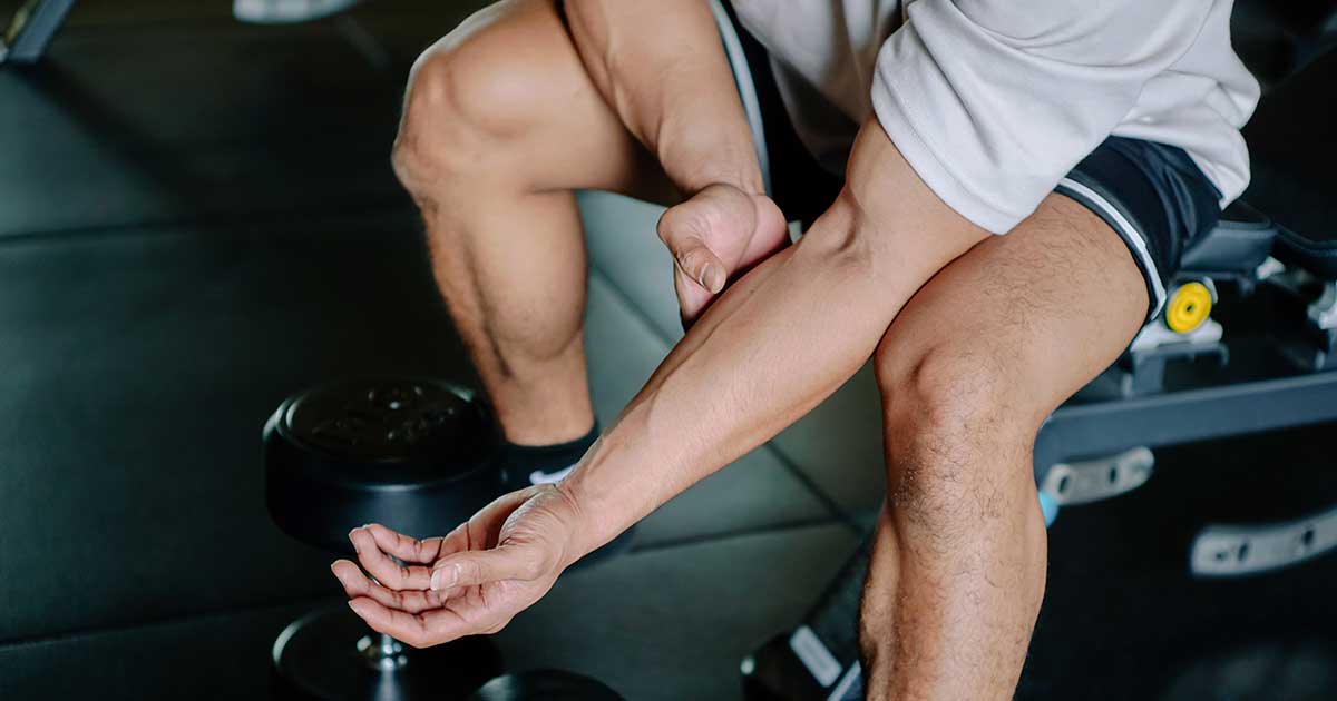 Mann im Fitnessstudio mit Muskelkater hält seinen Unterarm nach dem Training.