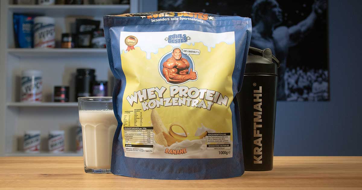 Rühls Bestes Whey Protein Konzentrat in der Sorte Banane mit Shaker und gemischtem Shake auf einem Tisch