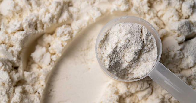 Löffel mit weißem Proteinpulver auf einer Oberfläche mit losem Pulver – Symbolbild zur Haltbarkeit und Lagerung von Eiweißpulver