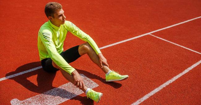 Erschöpfter Athlet nach dem Training sitzt auf der Bahn – Symbol für Regeneration im Leistungssport