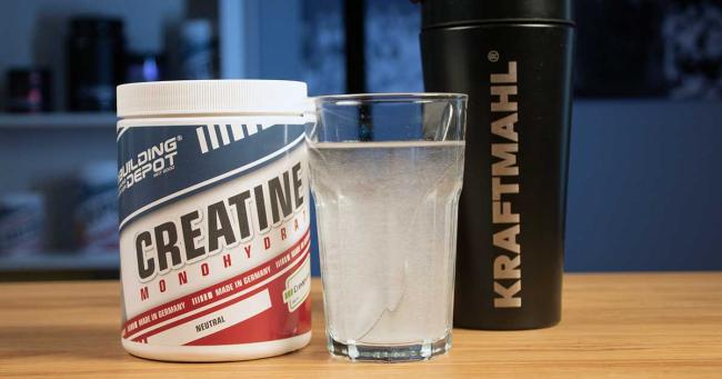 Creatin Monohydrat mit Glas und Kraftmahl Shaker auf Holztisch