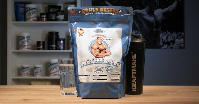 Beutel Rühls Bestes Cluster Dextrin neben Kraftmahl Shaker und Wasserglas auf Holztisch