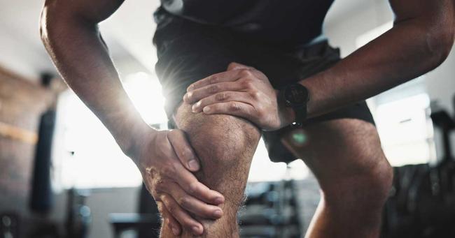 Sportler hält sich beim Training das Knie – Schmerzen nach körperlicher Belastung
