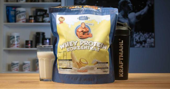 Rühls Bestes Whey Protein Konzentrat in der Sorte Banane mit Shaker und gemischtem Shake auf einem Tisch