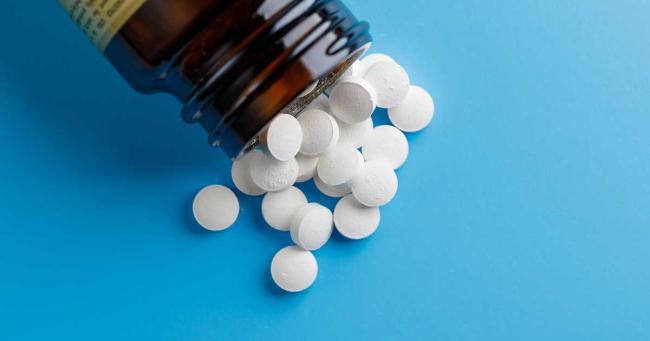 Weiße Zinktabletten, die aus einer braunen Supplementflasche auf einen blauen Hintergrund fallen.