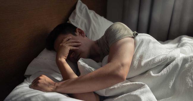 Mann liegt morgens müde im Bett und kommt schwer aus dem Schlaf