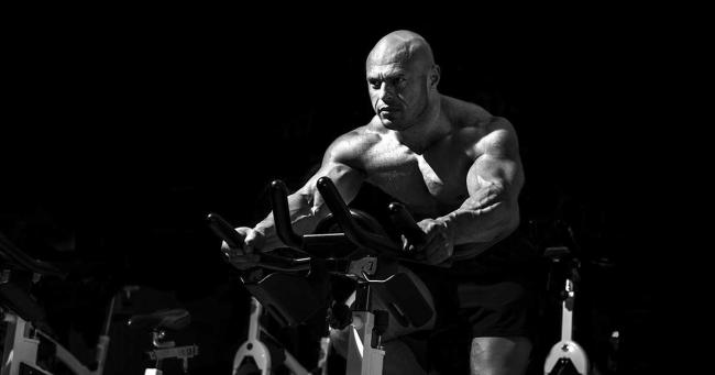 Muskulöser Kraftsportler beim Cardio-Training auf dem Bike im Fitnessstudio