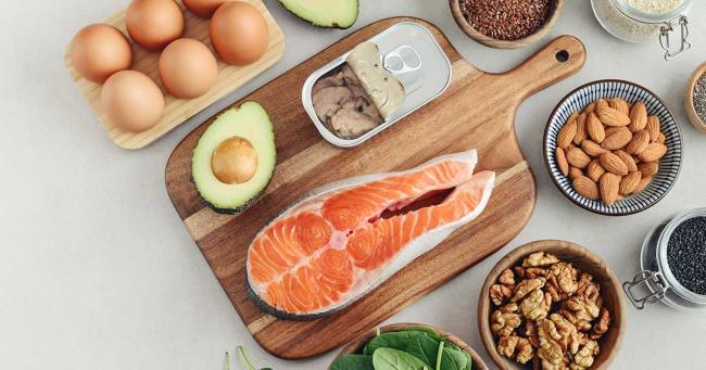 Gesunde Fettquellen wie Lachs, Eier, Avocado und Nüsse auf einem Tisch