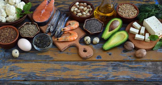 Omega-3-reiche Lebensmittel wie Fisch, Nüsse, Samen und Avocado auf einem Holztisch