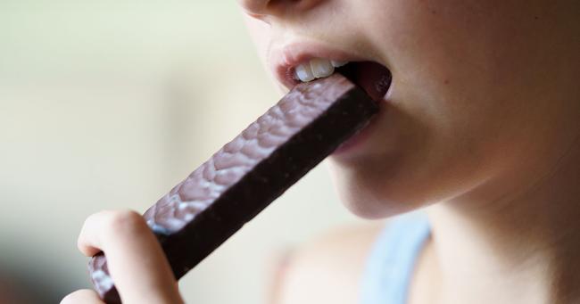Person isst einen Proteinriegel als Snack während einer kalorienbewussten Ernährung.