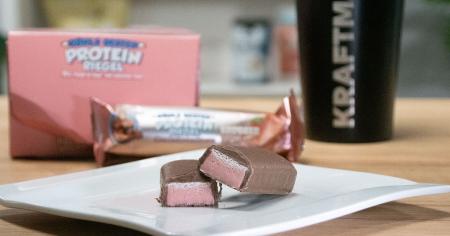 Angeschnittener Rühl24 Protein-Riegel Erdbeer-Creme mit rosa Füllung und Schokoladenüberzug im Produkttest.
