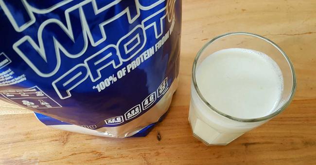 Bild zeigt 100 % Whey Protein von Scitec Nutrition und ein Glas mit Proteinshake