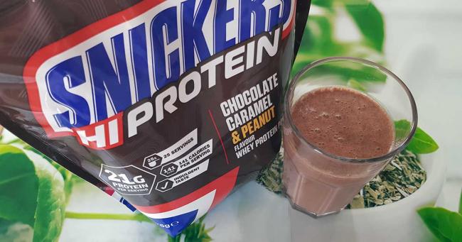 Bild zeigt Snickers Protein Pulver Packung und ein Glas mit Shake