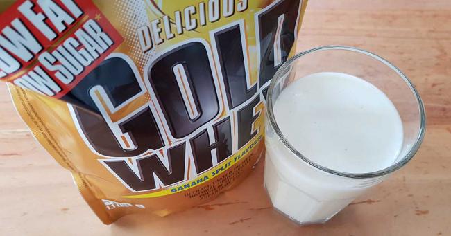 Bild zeigt Weider Gold Whey und ein Glas des zubereiteten Proteinshakes